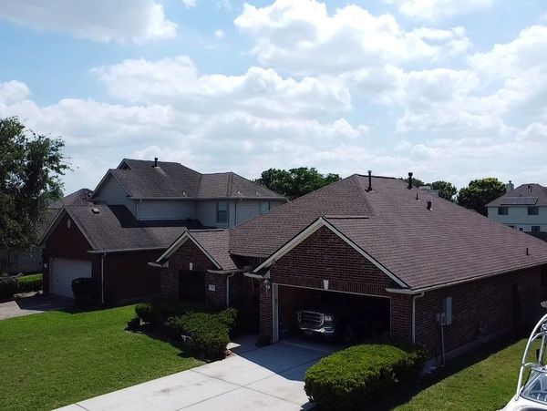Suburban brick houses with green lawns under a partly cloudy sky.Houston roofing services, roofing installation, and roof inspections from storms.