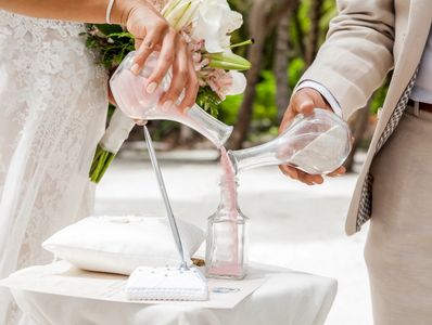 Bride and groom pouring colorful different colored sands into the crystal vase close up