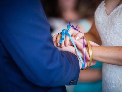 Close up picture of bride and groom's hands tied with colorful blue