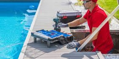 Technician repairing pool equipment near a swimming pool.
