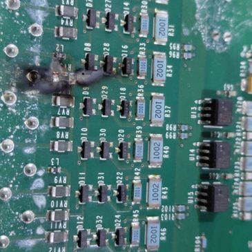 Close-up of a damaged circuit board with burnt components and resistors.