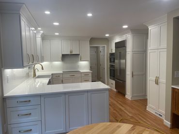 Renovated kitchen with white cabinets, slab backsplash, hardwood floors, stainless steel appliances