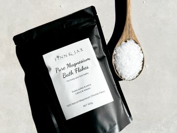 Black pouch of pure magnesium bath flakes with a wooden spoon filled with flakes.
