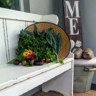 Fresh garden vegetables and flowers arranged on a rustic white bench.