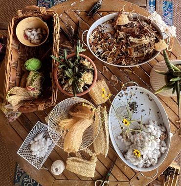 A rustic table with cotton, dried plants, loofahs, and yarn for crafts.
