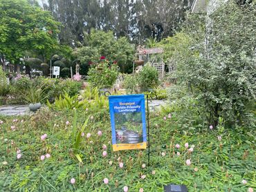 A lush Florida-friendly garden with a blue recognition sign and various plants.