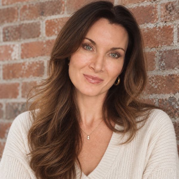 Smiling woman with long brown hair against a brick wall.