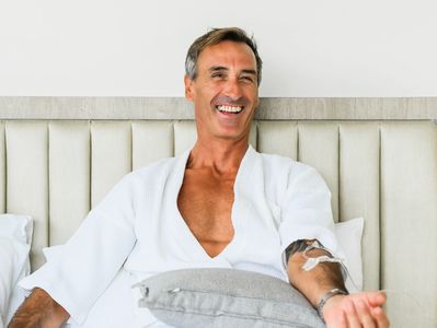 A happy man getting an IV drip while laying in a luxury hotel bed in Bangtao, Phuket