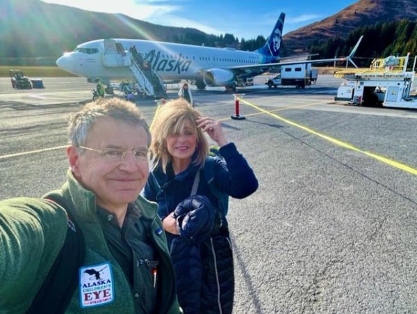 Two travelers take a selfie near an Alaska Airlines plane.