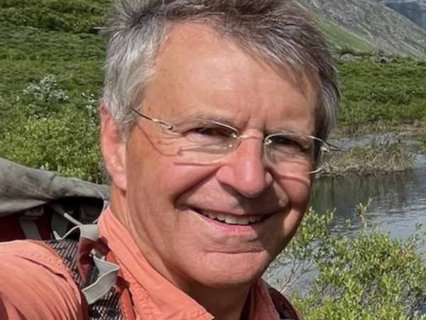 Smiling man with glasses outdoors near a river.