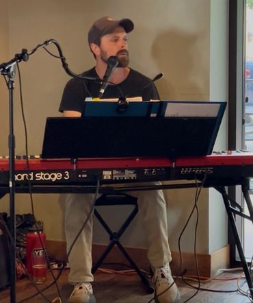 Man playing keyboard and singing into a microphone indoors.