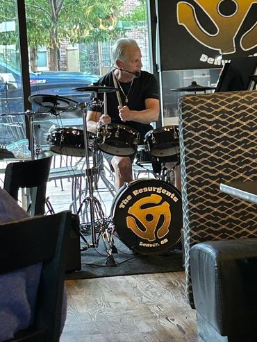 A man plays drums in a cozy indoor setting with natural light.