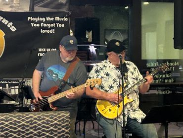 Two musicians playing guitars on stage with a backdrop sign.