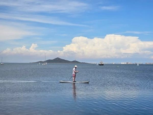 A person paddleboarding on calm waters with a scenic island and cloudy sky in the background.