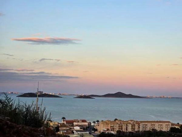 Calm sea with islands and city skyline at sunset.