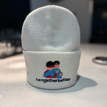 White beanie with embroidered hugging figures and "twogetherbetter" text.