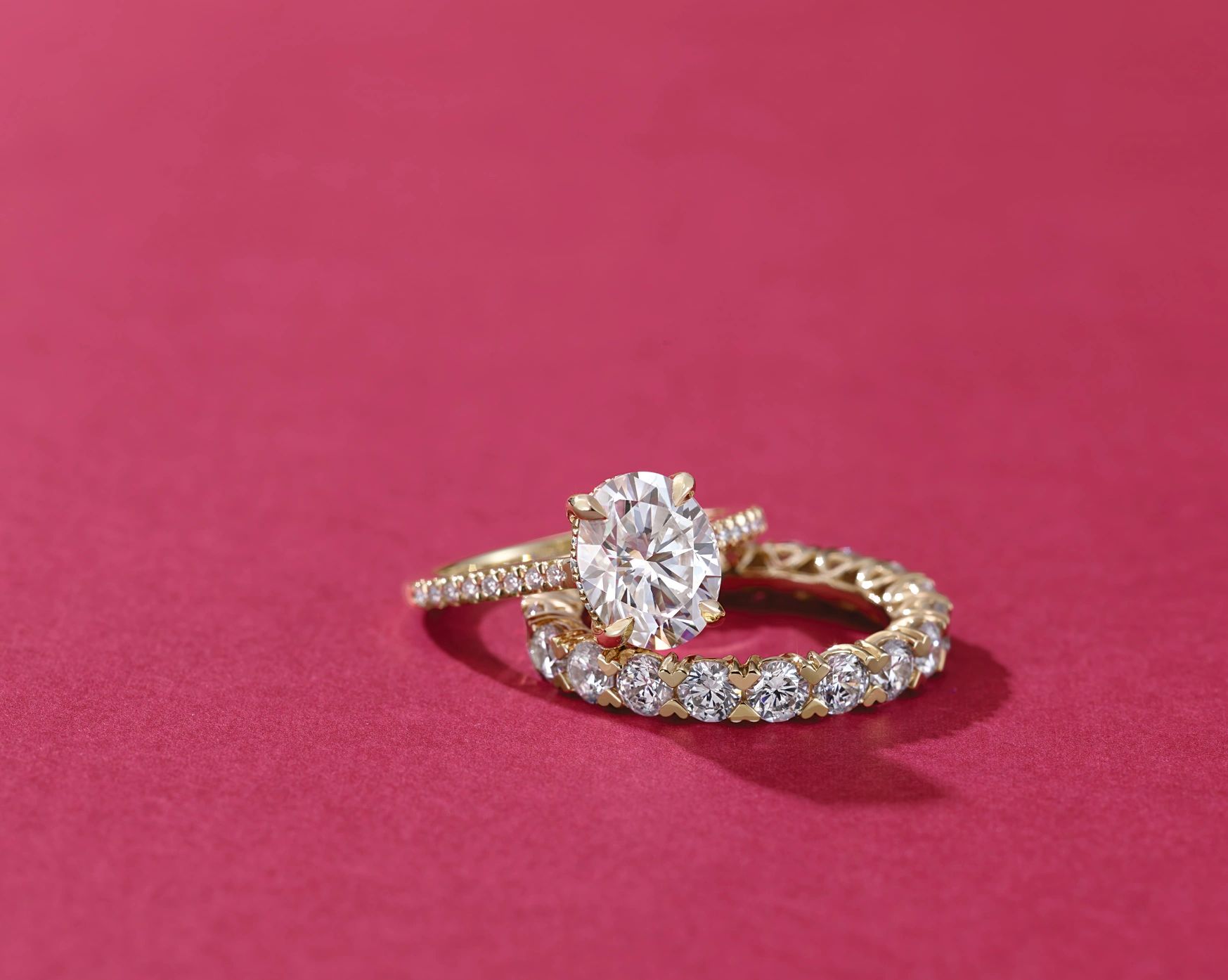 Oval Diamond Engagement ring paired with a gold diamond wedding band on a red background.