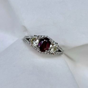Finished custom ring with an oval red center stone and diamond halo.