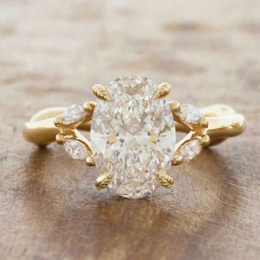 Gold engagement ring with a large oval natural diamond and marquise diamond side accents.