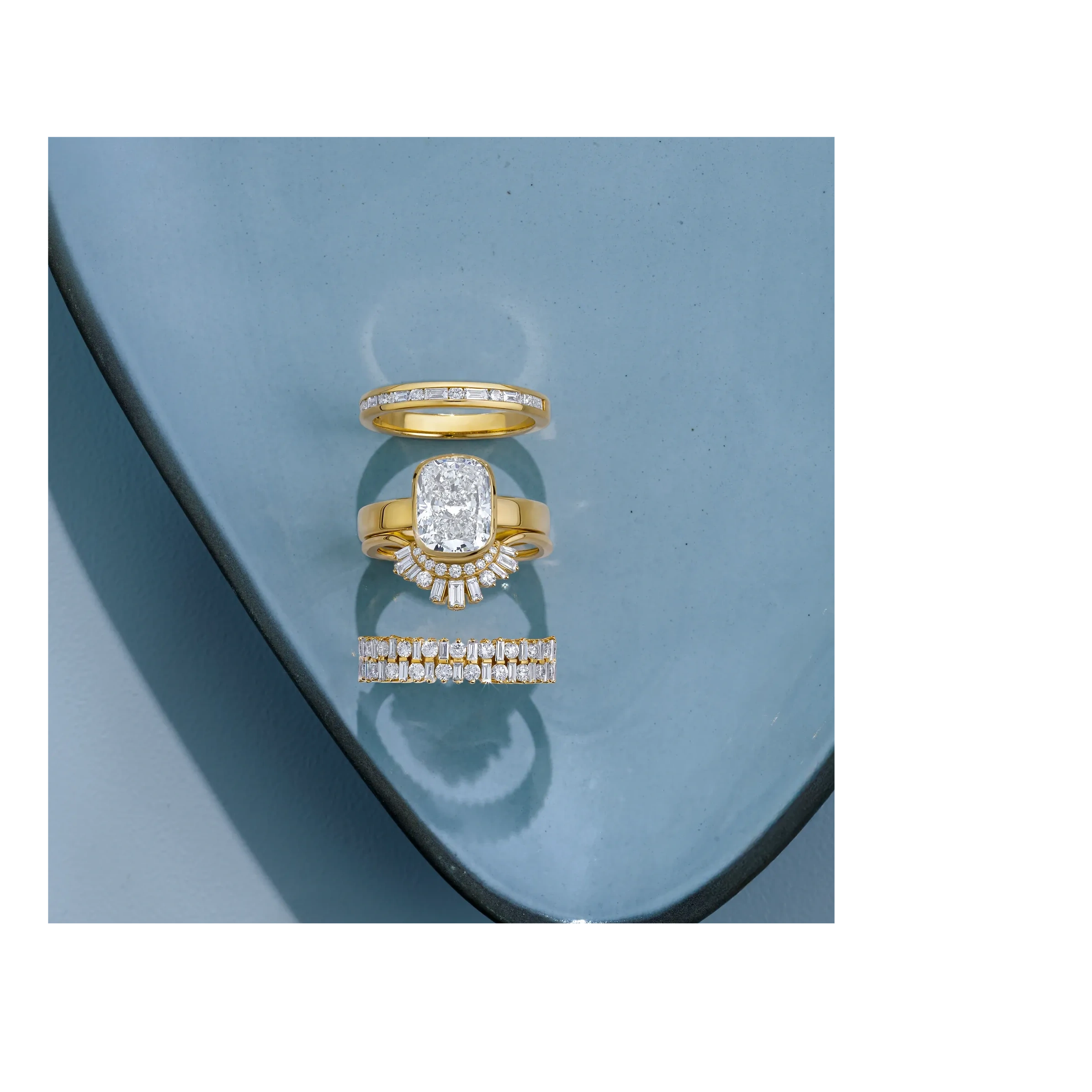Stack of custom gold and diamond engagement rings featuring an oval center diamond.