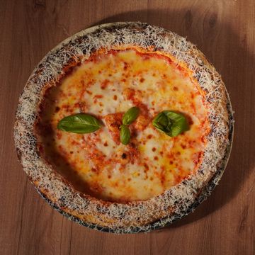 A cheese pizza with a crust coated in grated cheese and topped with basil leaves.