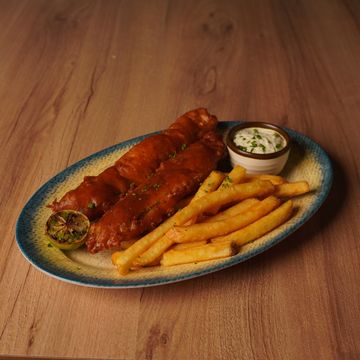 Plate of fish and chips with tartar sauce and grilled lemon on wooden table.