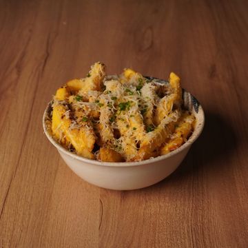 Bowl of cheesy fries garnished with herbs on wooden table.