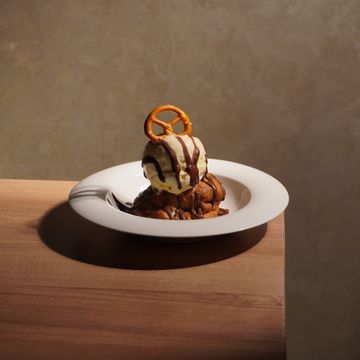 Ice cream scoop with chocolate drizzle and pretzel on white plate.