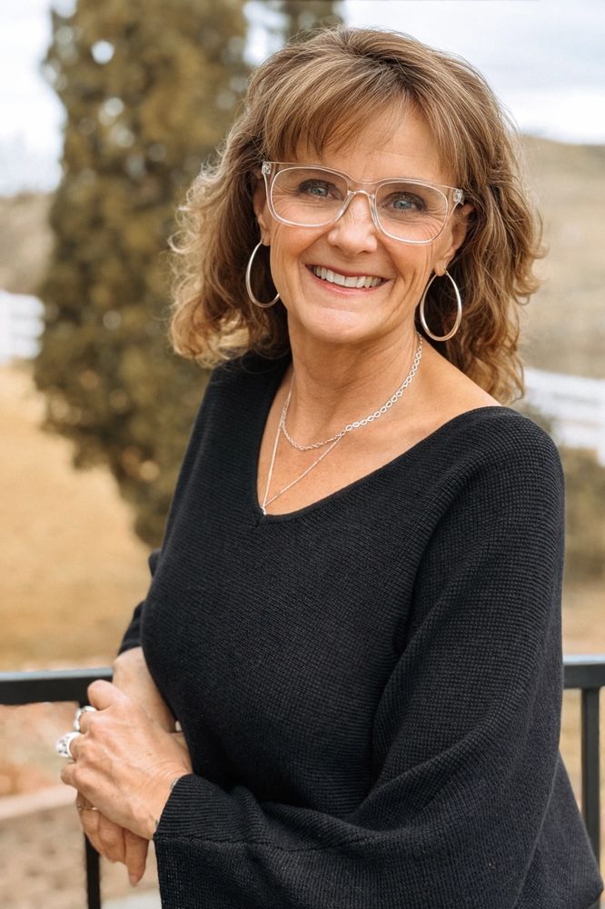 Smiling woman in glasses and black sweater outdoors.