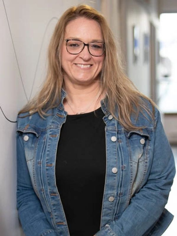 Femme souriante en veste en jean et lunettes.