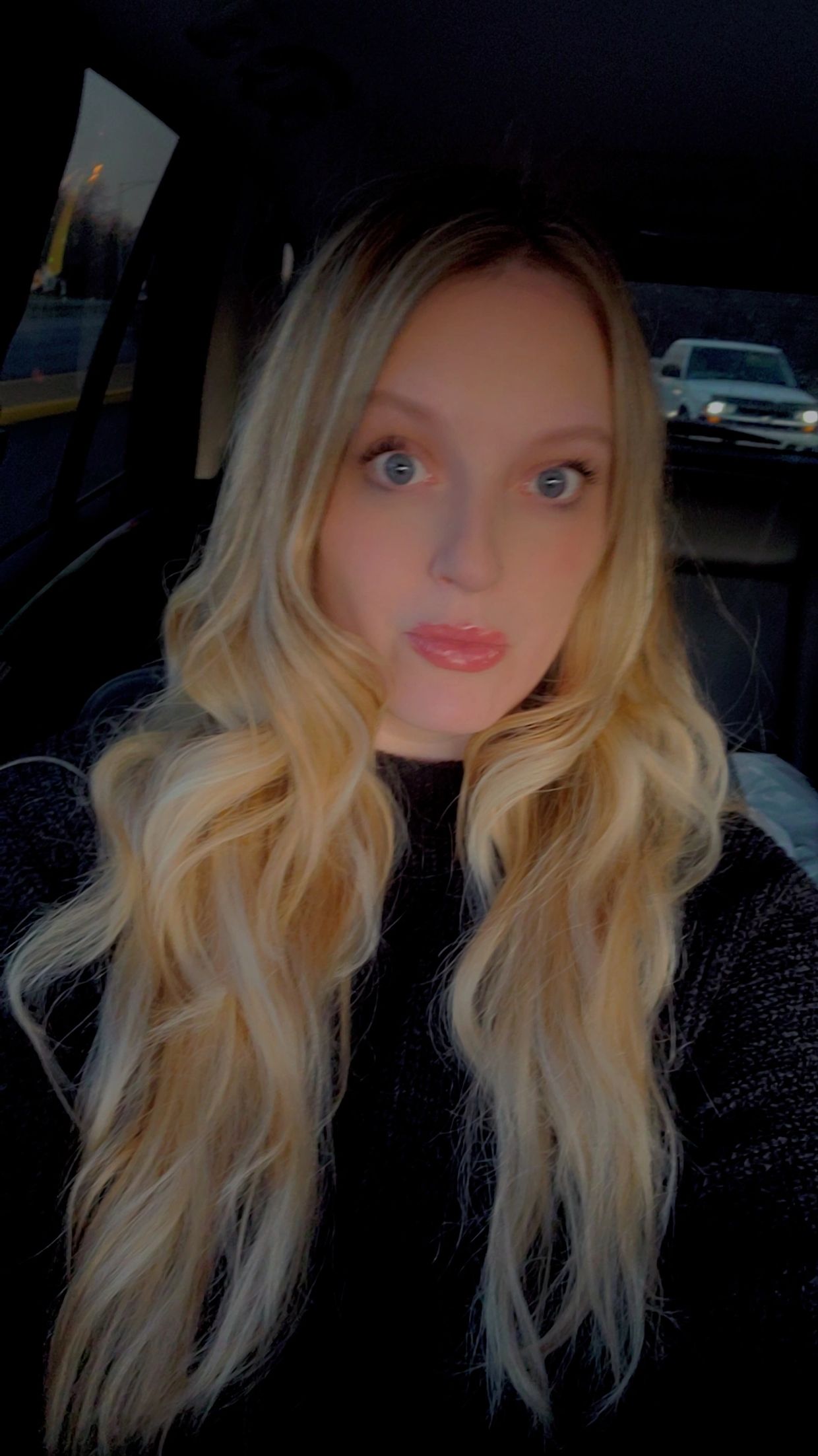 A woman with blonde hair and blue eyes in a car.