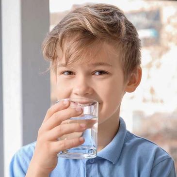 a happy boy holding a glass of water in front of his mouth