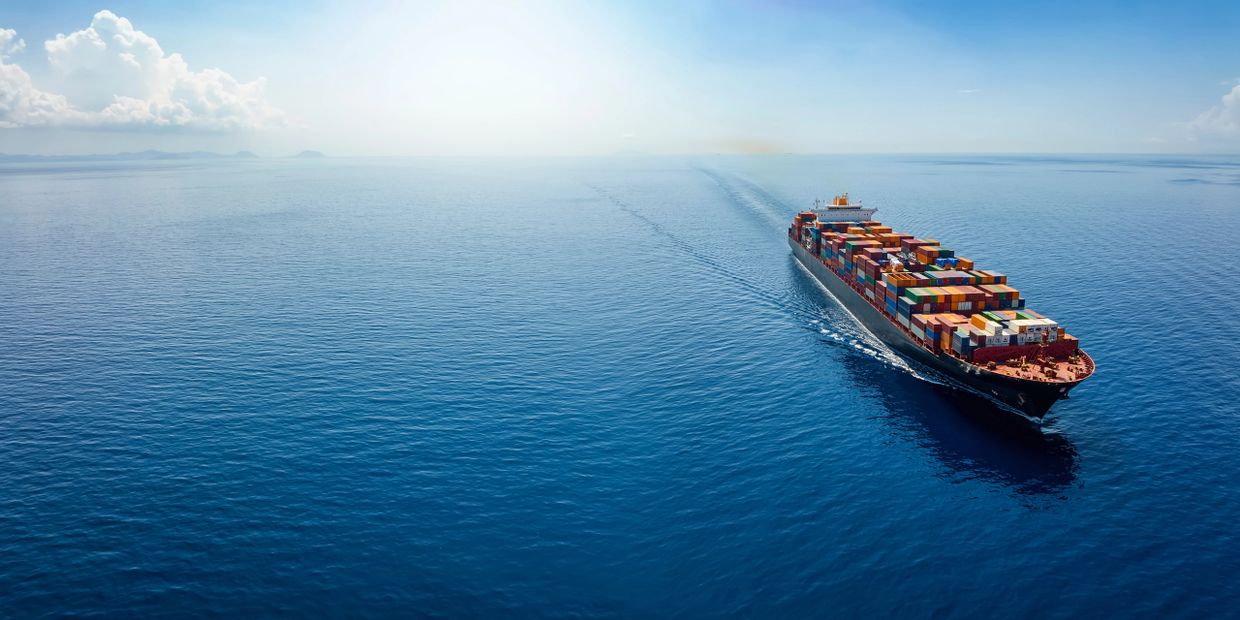 A large container ship sailing on a calm, vast ocean under a clear blue sky.