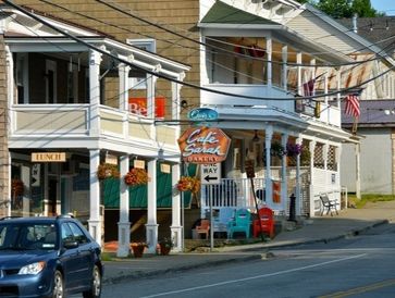 Charming small-town street with a bakery and colorful chairs outside.
