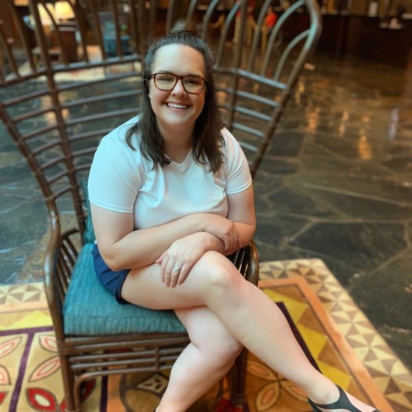 Smiling woman in glasses sitting on a wooden chair indoors.
