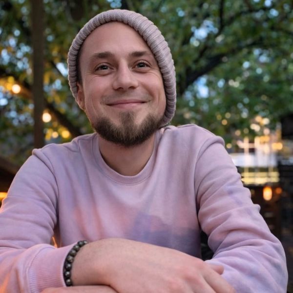 A smiling man in a beanie and sweatshirt outdoors.