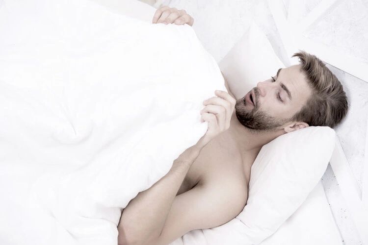 Man in bed lifting duvet to look at his penis