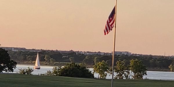 Sailboat on a lake at sunset with an American flag in the foreground.