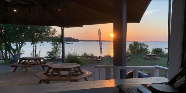 Sunset view over picnic tables by the water under a shaded pavilion.