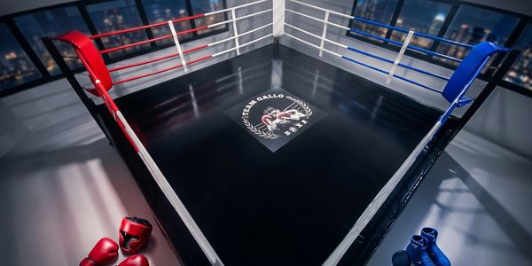 Empty boxing ring with red and blue corners and gear on the floor.