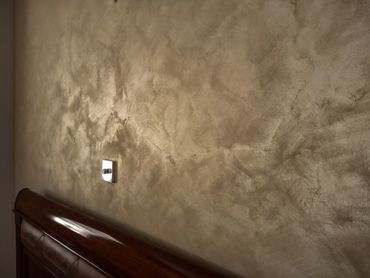 Textured beige wall with a wooden bed headboard and a dimmer switch.