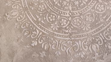 Close-up of intricate floral and geometric stucco pattern on a textured wall.