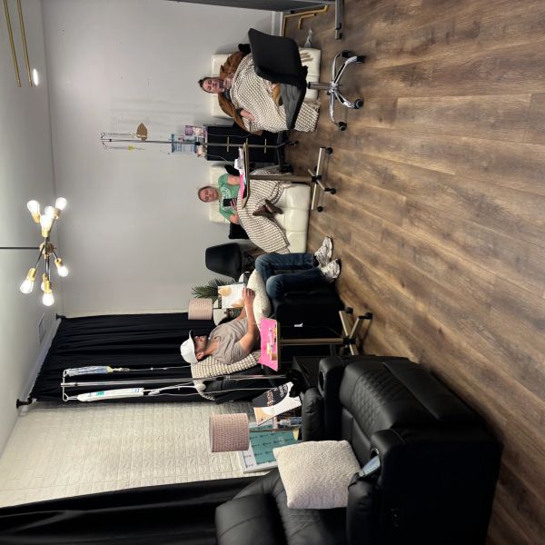 Three people receiving IV treatments in a modern clinic room with cozy chairs and warm lighting.