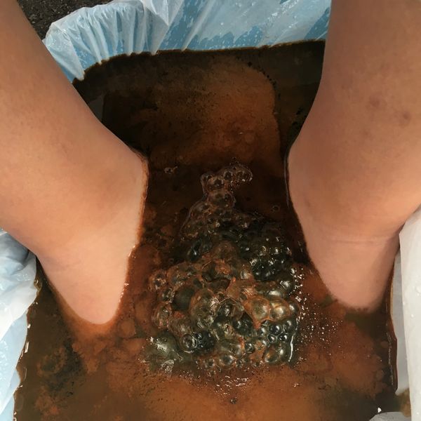 Feet soaking in a dark, fizzy liquid.