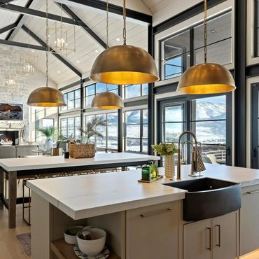 Modern kitchen with large windows and mountain views, featuring pendant lights and a stone fireplace.