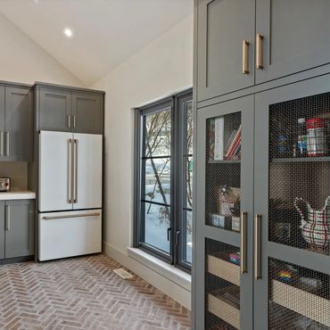 Modern kitchen with gray cabinets, white countertops, and a large window showing a snowy outdoor view.