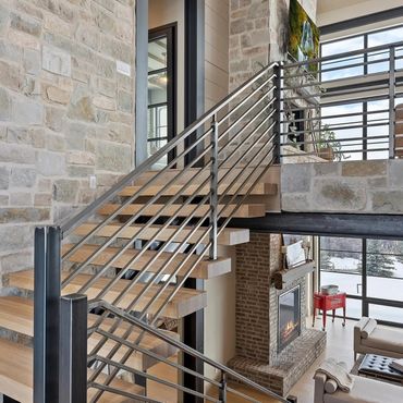 Modern staircase with wooden steps and metal railing in a cozy living room with stone walls.