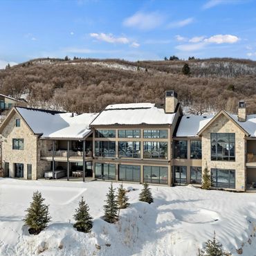 Luxury mountain home covered in snow with large windows and balconies.