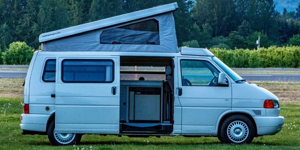White camper van with pop-up roof and open sliding door on grass.