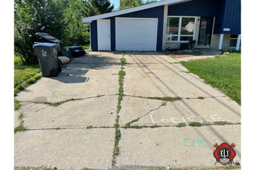 Cracked concrete driveway with grass growing through and chalk markings.